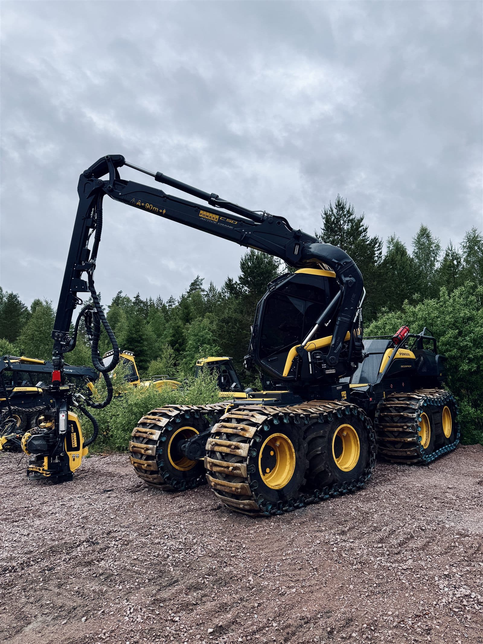Ponsse Scorpion-skördare med kran och aggregat uppställd på grusplan framför skogen